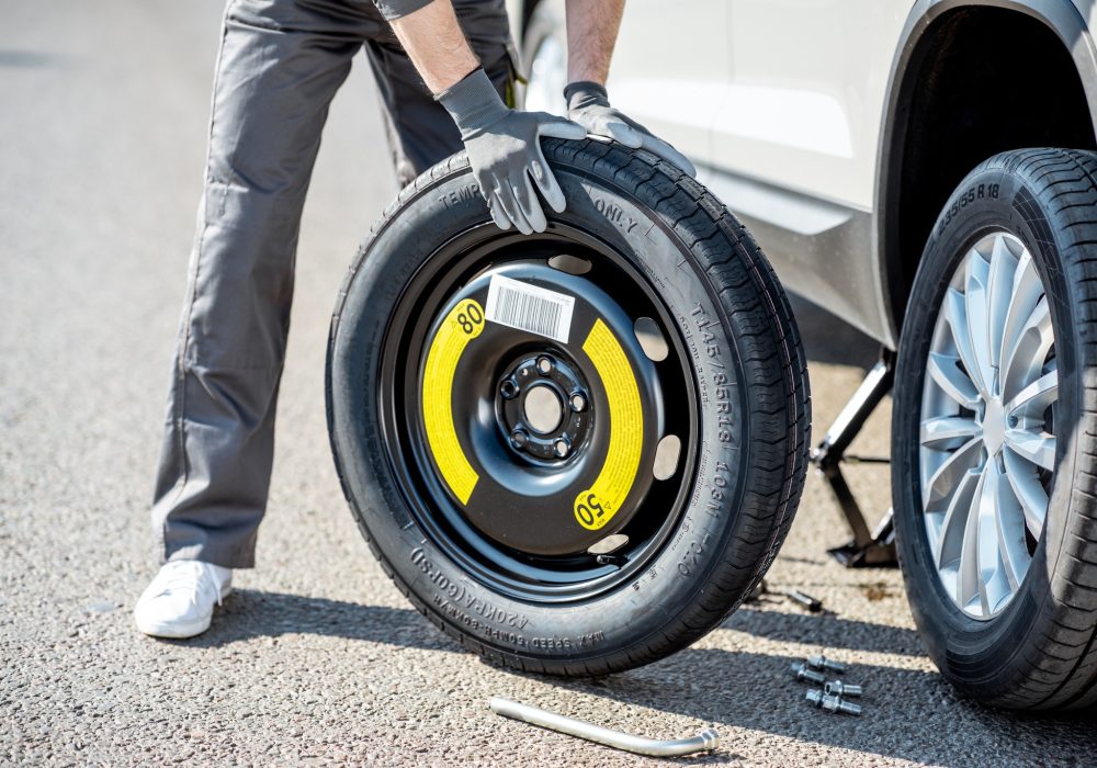 Road assistance worker in uniform changing car wheel on the highway, close-up view